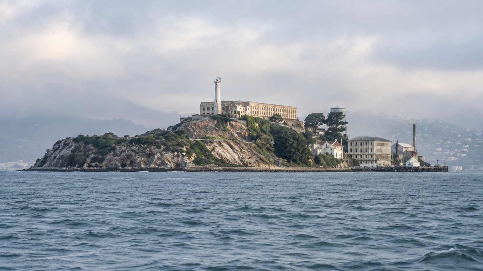 L'isola di Alcatraz nella baia di San Francisco, con il faro e l'edificio del penitenziario sulla roccia, vista dall'acqua in una giornata di leggera foschia