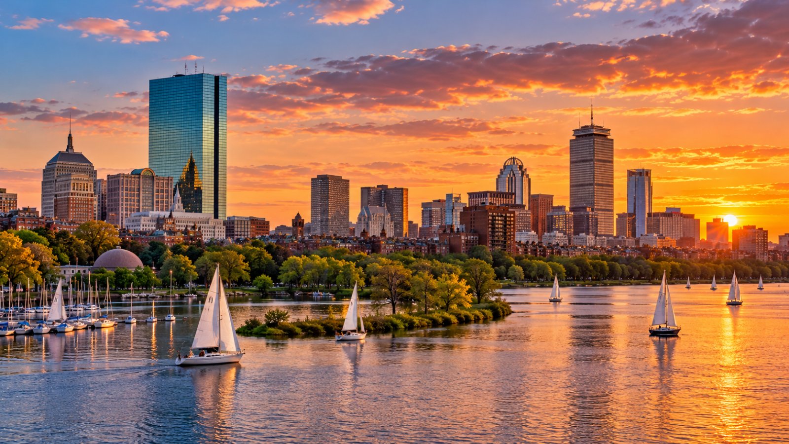 Lo skyline di Boston visto dal fiume Charles al tramonto, con barche a vela e alberi lungo la riva