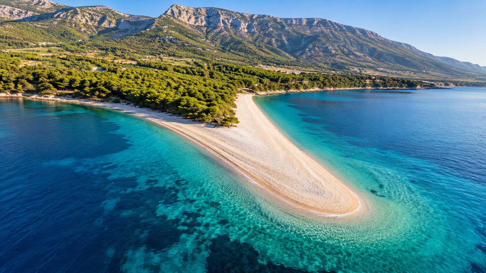 La spiaggia di Zlatni Rat a Bol vista dall'alto: una lingua di ciottoli chiari che si allunga nel mare turchese, con la pineta alle spalle e il monte Vidova gora sullo sfondo