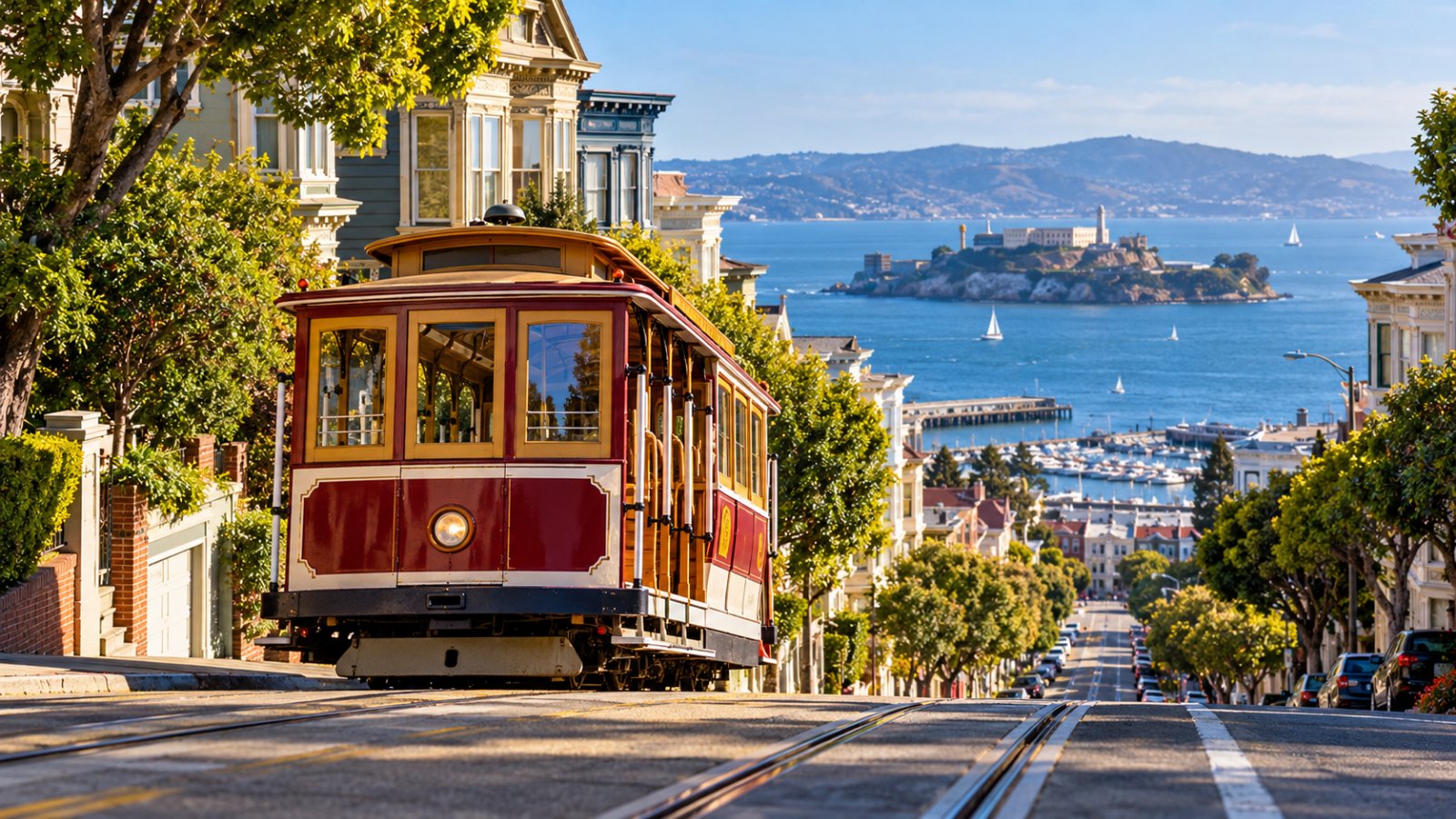 Un cable car in legno rosso e crema sale lungo una strada ripidissima di San Francisco, con la baia e l'isola di Alcatraz sullo sfondo