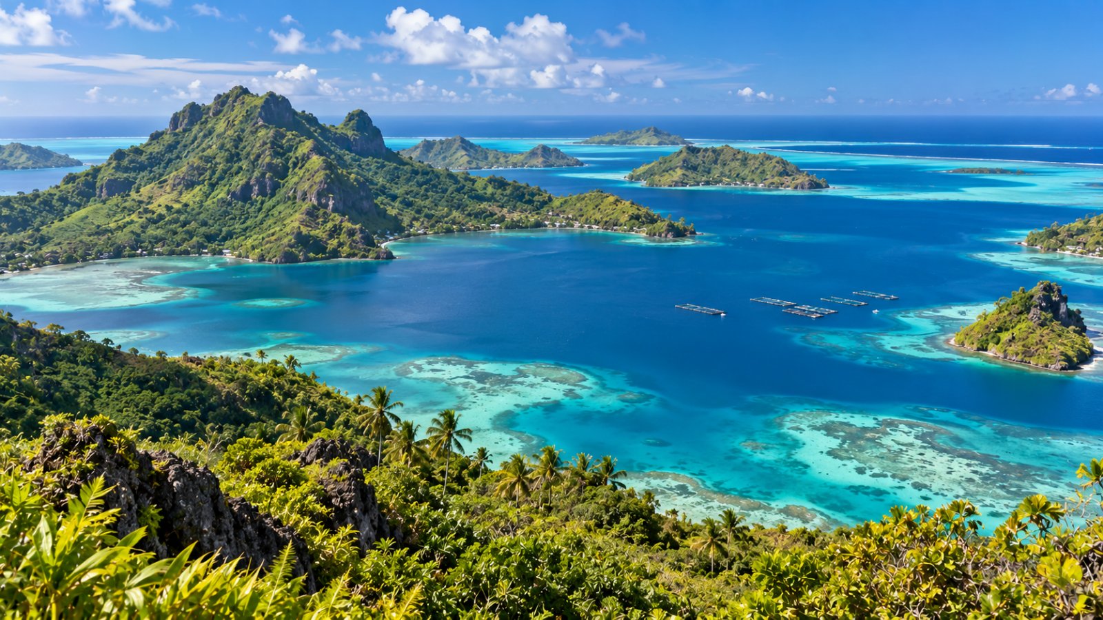 La laguna delle isole Gambier vista dalle alture di Mangareva, con acqua turchese e blu, isole alte e verdi, motu all'orizzonte e piccole piattaforme di una fattoria di perle