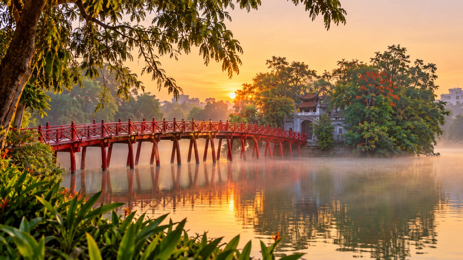 Il ponte rosso The Huc che attraversa il lago Hoan Kiem verso il tempio Ngoc Son, all'alba con una leggera foschia sull'acqua