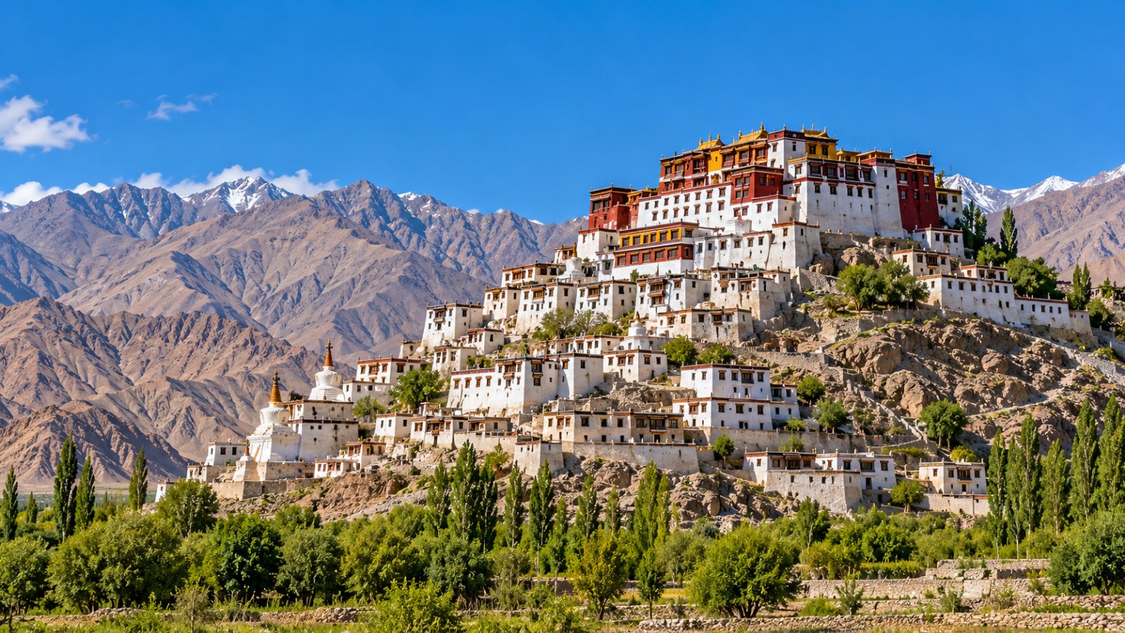 Il monastero di Thiksey con i suoi edifici bianchi e rossi a terrazze su una collina rocciosa, sotto un cielo blu intenso e con le montagne aride del Ladakh sullo sfondo