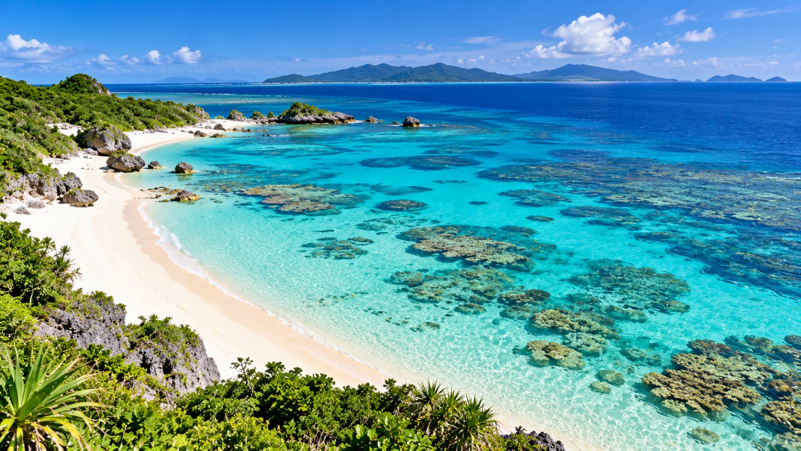 Una spiaggia di sabbia bianchissima con il mare turchese e trasparente sopra la barriera corallina, sotto un cielo azzurro con poche nuvole, in un'isola di Okinawa
