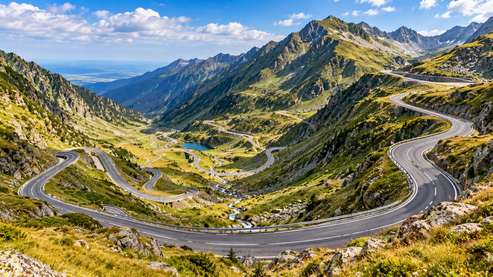 Una strada di montagna a tornanti che sale lungo un versante verde fino a un passo roccioso