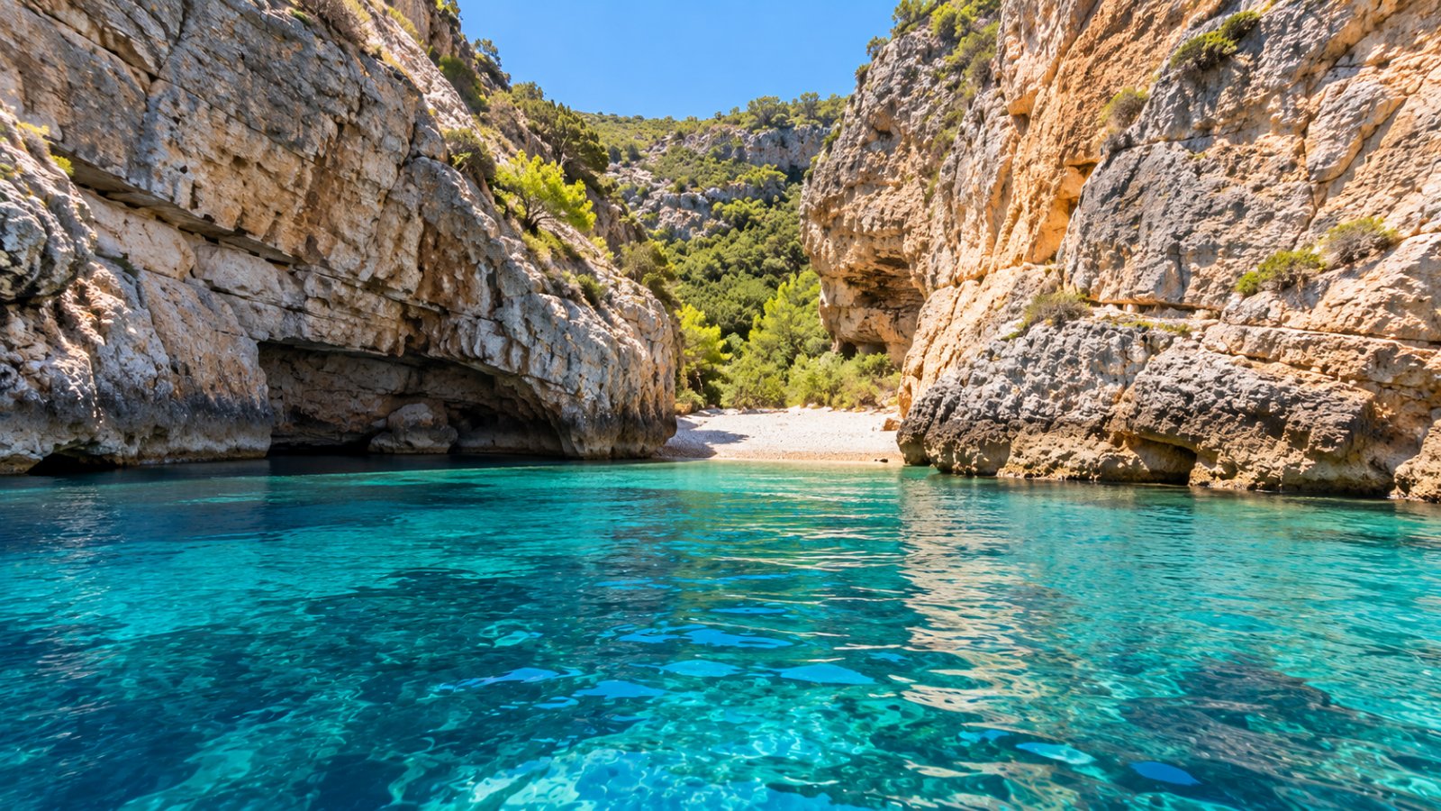 La baia di Stiniva sull'isola di Vis, con alte pareti di roccia che chiudono una piccola spiaggia di ciottoli e l'acqua limpidissima, vista dal mare verso la stretta apertura della baia