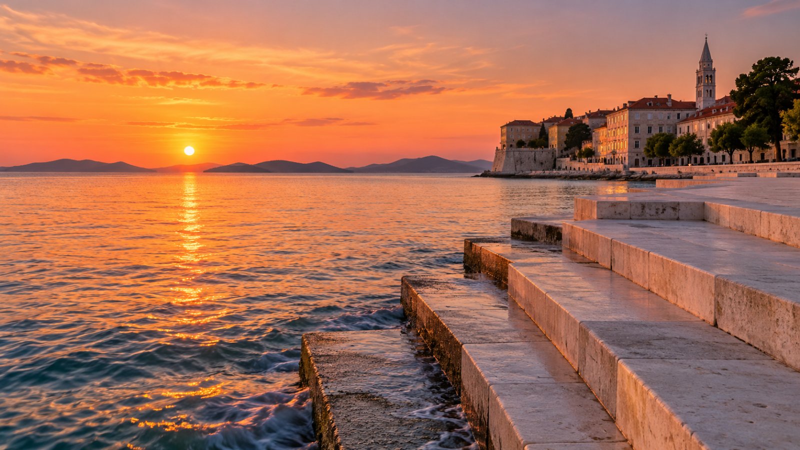 Il lungomare di Zara al tramonto, con i gradini di pietra bianca dell'Organo marino che scendono in acqua e il campanile della cattedrale sullo sfondo